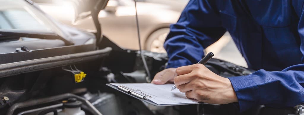 Mechanic in navy overalls writing on a clipboard beside an open engine bay